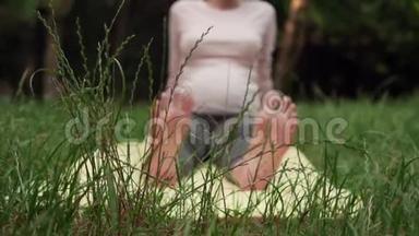 孕妇在公园里用地毯做瑜伽，双腿伸直，做脚的热身。